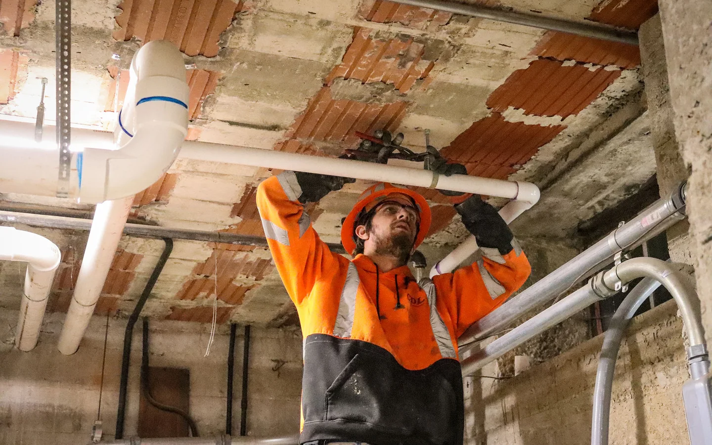 Plumber installing overhead piping in a commercial mechanical space