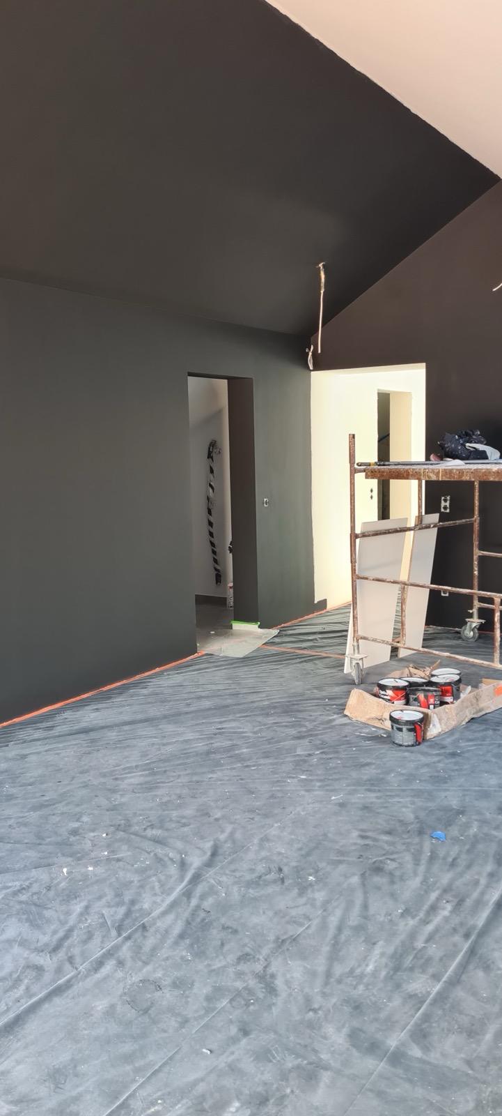 Interior painting of dark grey walls and a sloped ceiling with protected floors