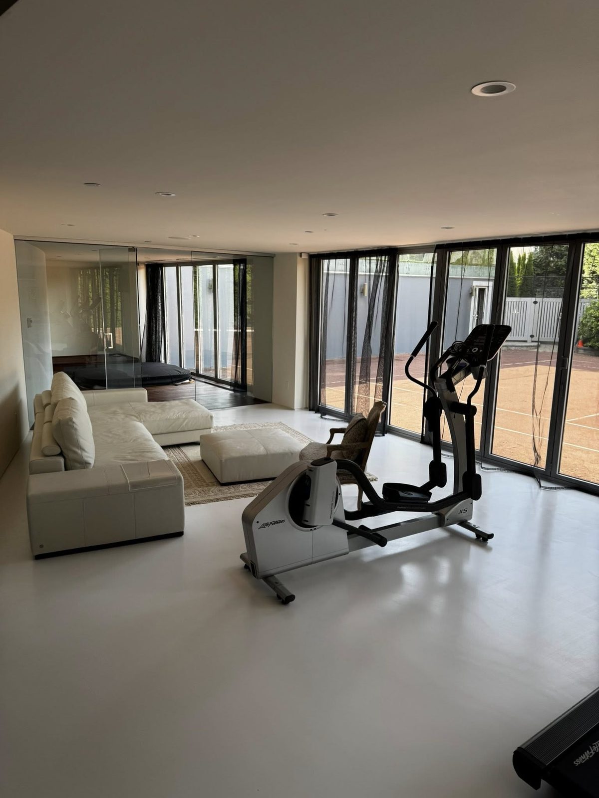 Finished home gym and living area with floor-to-ceiling glass overlooking the tennis court in a Jericho Beach estate