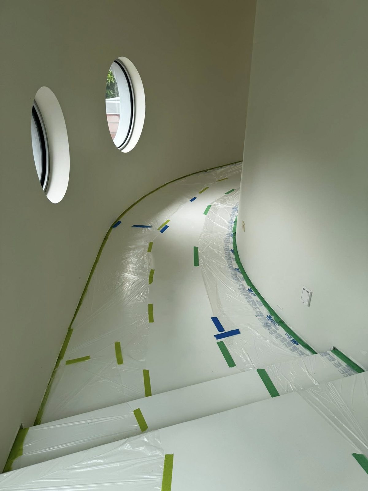 Curved stairwell with round porthole windows masked for interior painting in a luxury Jericho Beach estate, Vancouver