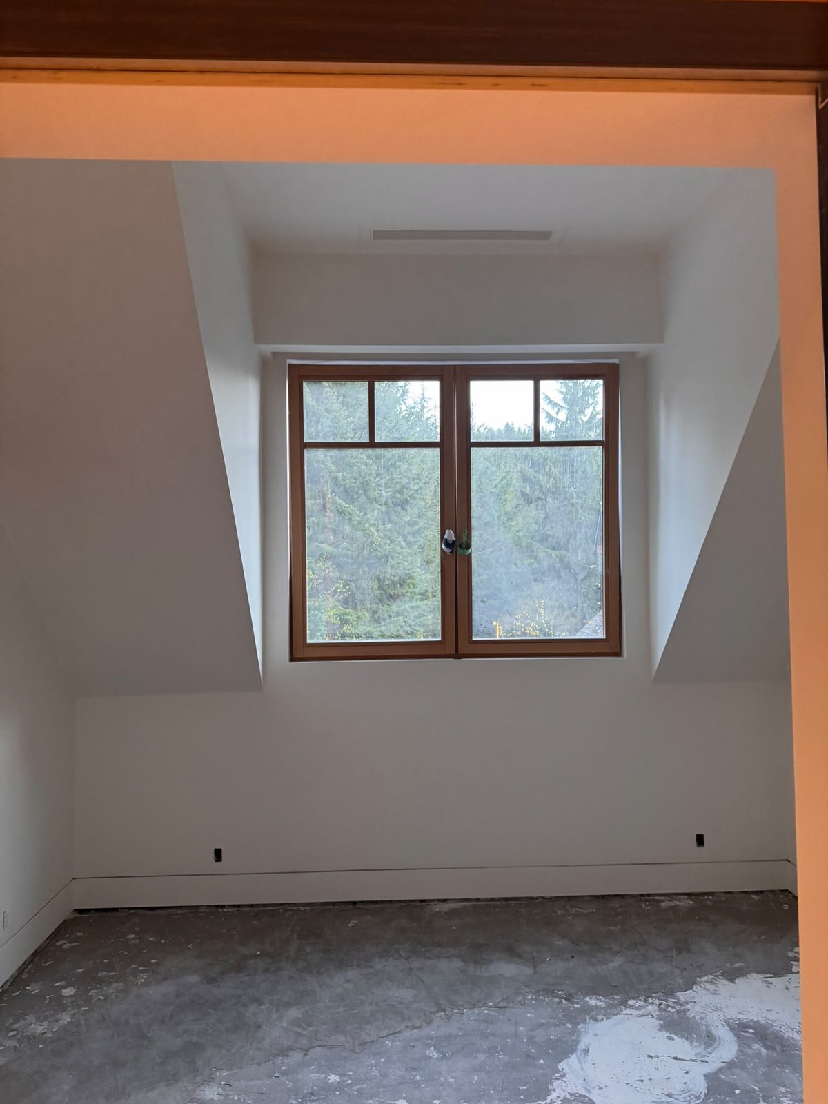 Finished smooth white Level 5 walls and angled ceiling with a wood-framed forest window in a renovated Whistler chalet