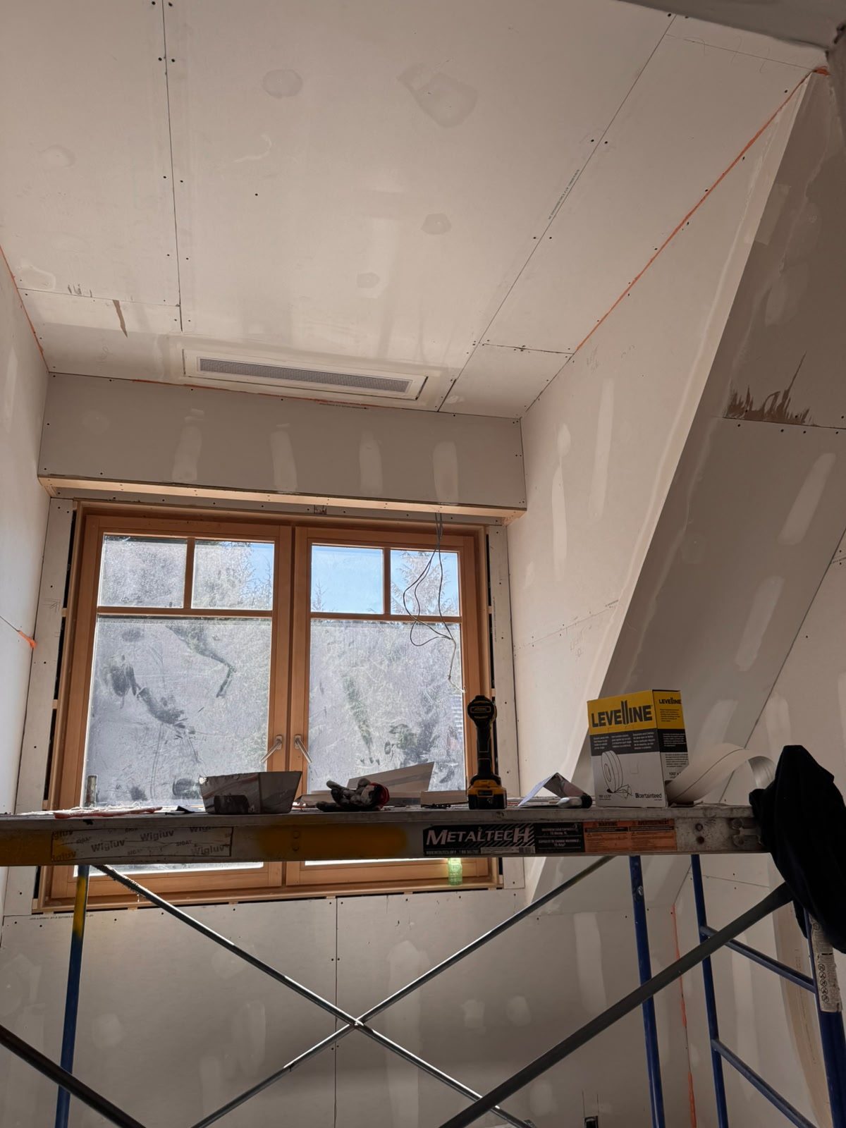 New drywall installed on the sloped ceiling around a wood-framed window in a Whistler chalet
