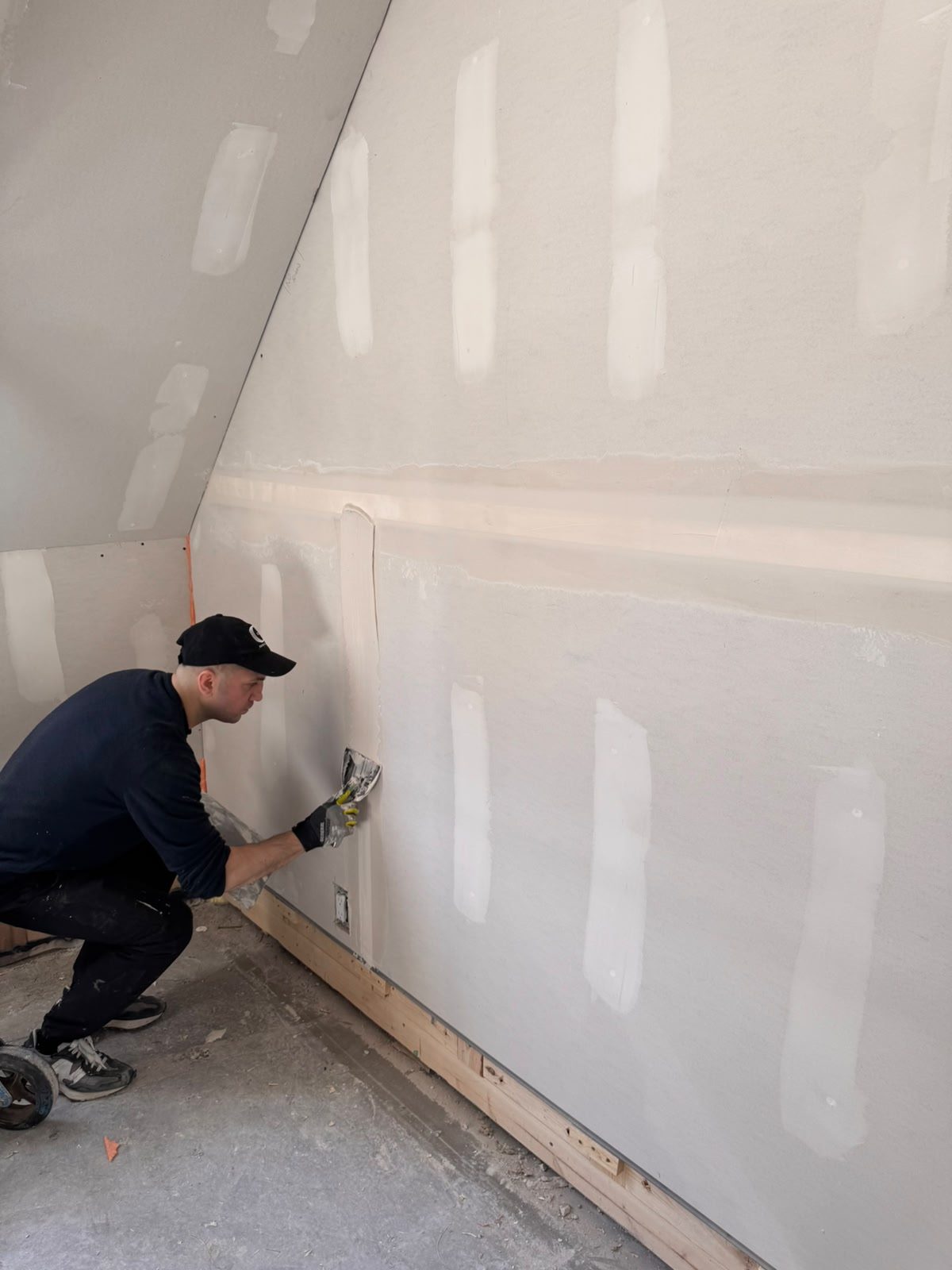 Worker applying a multi-coat skim finish to drywall joints on a sloped ceiling in Whistler