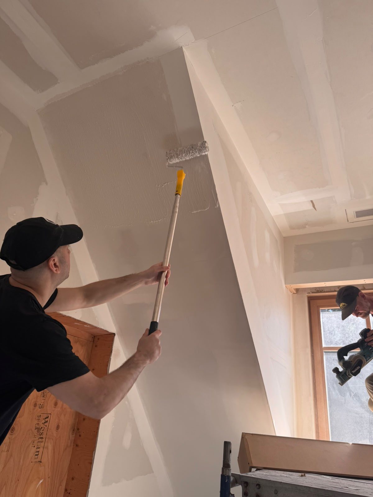 Worker rolling a finishing coat onto the sloped walls of a Whistler chalet interior renovation